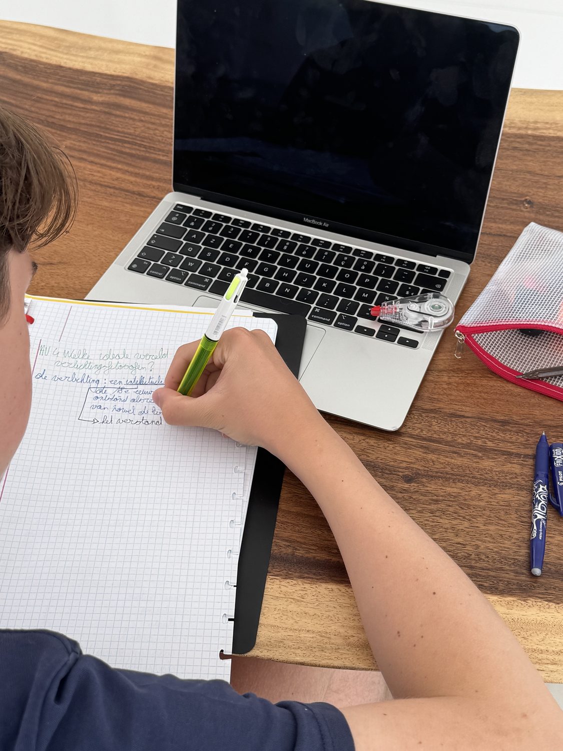 Leerling maakt notities naast een laptop en handboek